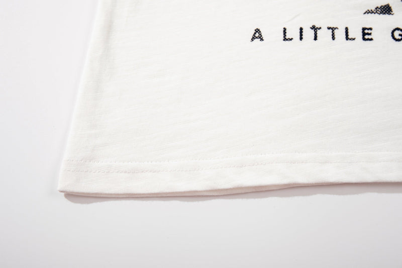 White graphic T-shirt hem with black punk text print reading A LITTLE G on soft cotton fabric