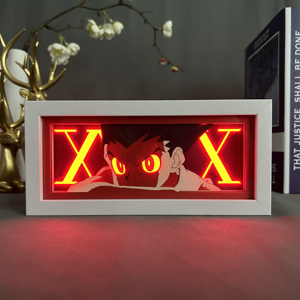 The Hunter × Hunter Anime Light Box showcases Gon Freecss with red eyes and a neon X theme, set against a dark backdrop. Nearby, find a small plant and an ornate deer statue beside a book titled &quot;THAT JUSTICE SHALL BE DONE.&quot; This 16-color LED piece embodies the intensity of *Hunter x Hunter*.