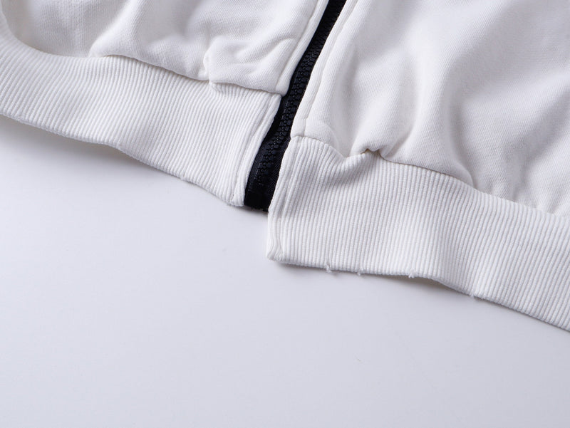 Close-up of white hoodie lower front with ribbed hem, black zipper, and gathered fabric near the pocket