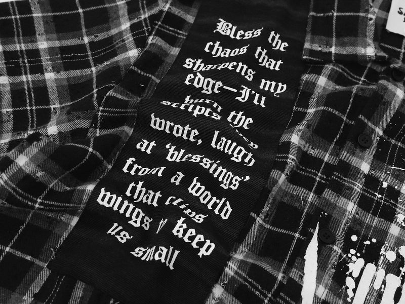 Black plaid streetwear shirt with gothic script graphic, distressed details, and button-up front panel with quote print
