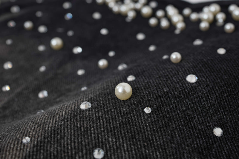 Close-up of black denim with pearl and clear rhinestone studs