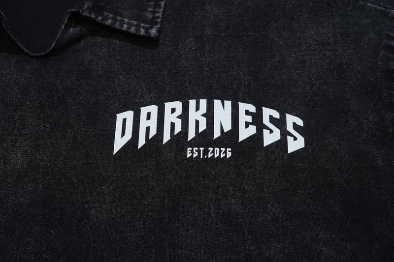 Black washed polo shirt with bold white darkness graphic and arched text across the chest