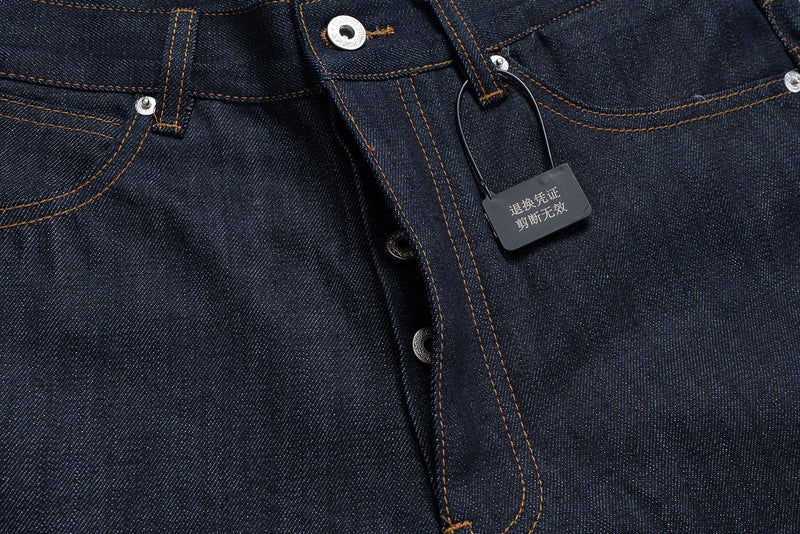 Close-up of front waistband, button fly and hanging tag on dark denim jeans