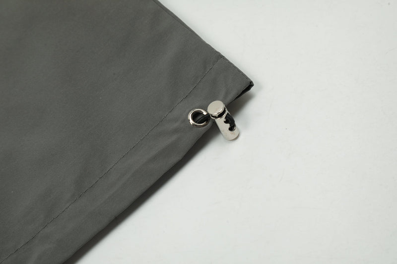 Close-up of hem drawstring and metal toggle on dark gray windbreaker