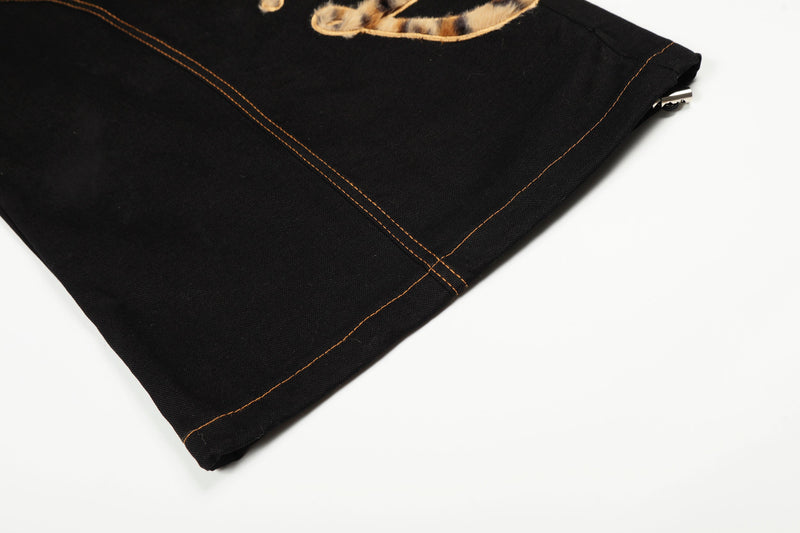Close-up of black pant hem with orange contrast stitching and small side zipper detail