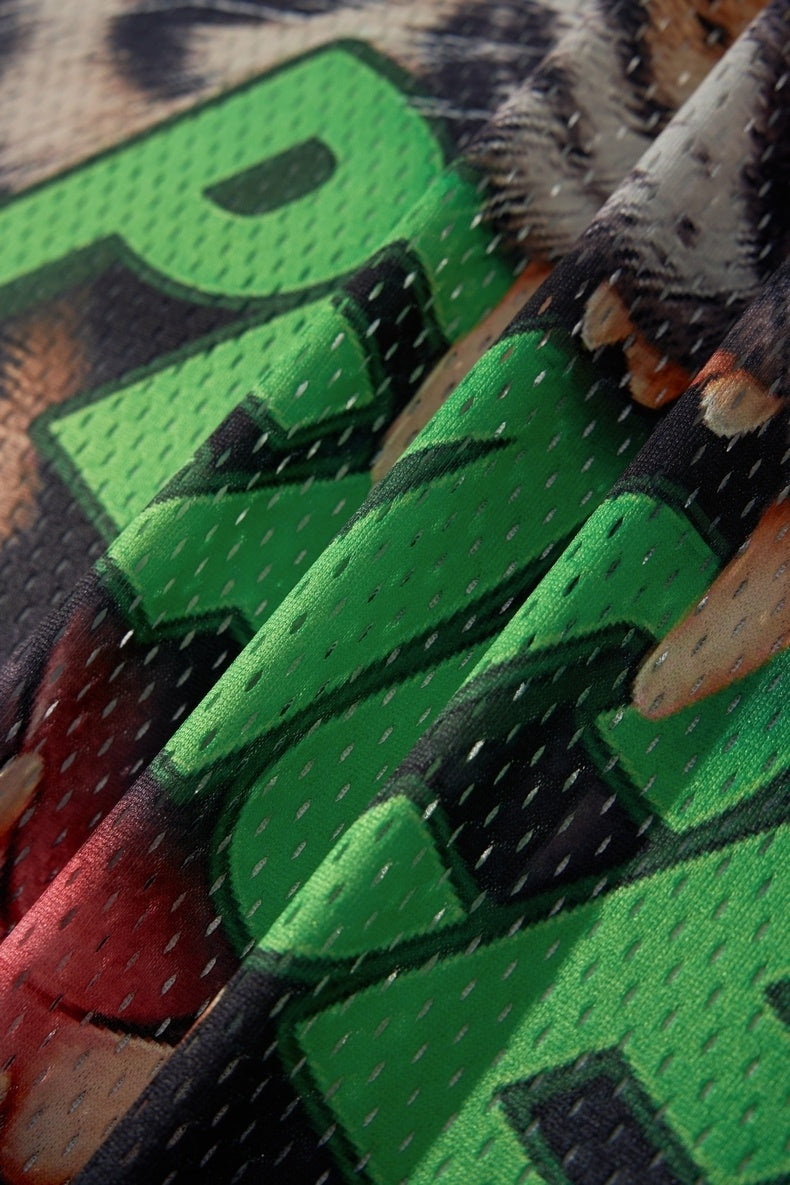 Close-up of green mesh jersey fabric with bold graphic lettering, tiger print accents, and textured streetwear details