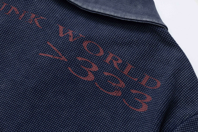 Close-up of a navy textured polo tee with faded red vintage graphic lettering and ribbed collar detail