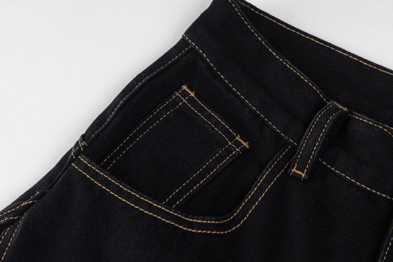 Close-up of the front pocket and waistband seam on black jeans with tan stitching