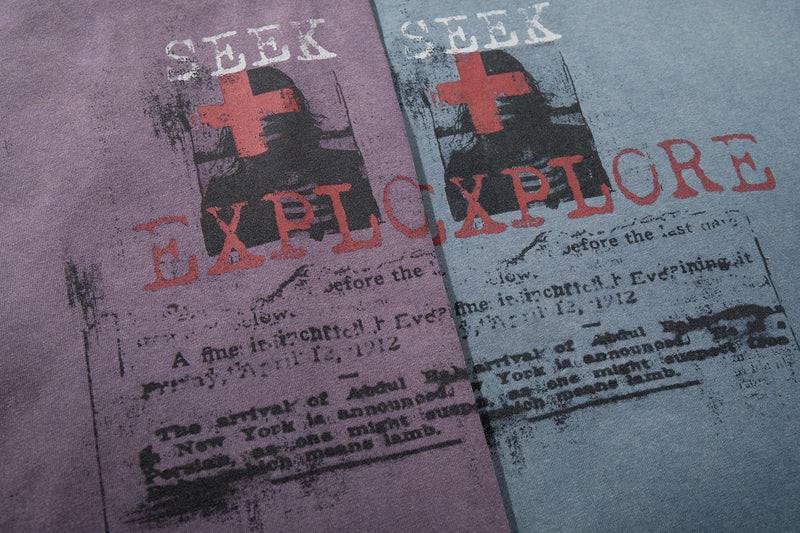 Close-up of vintage washed graphic T-shirts in purple and blue with Seek Explore print and distressed streetwear design