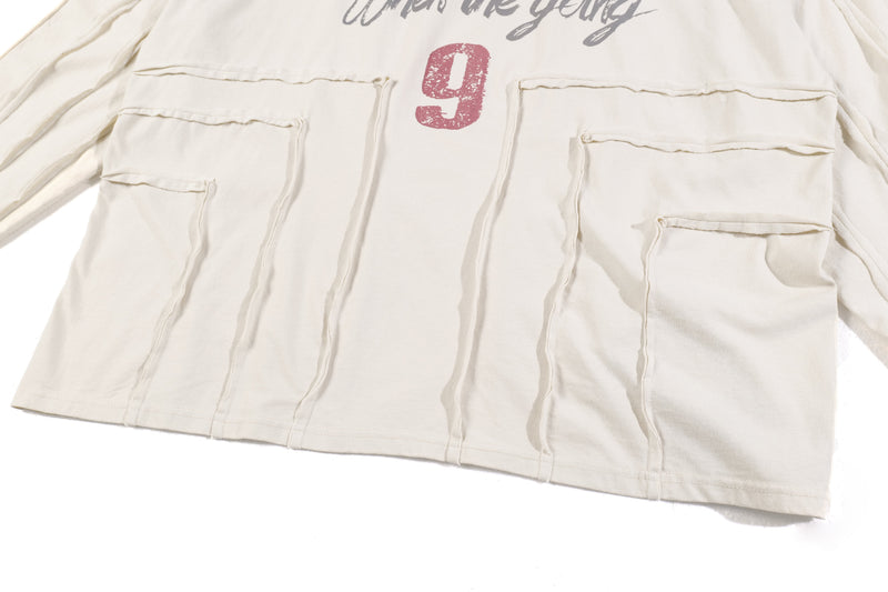 Lower front of cream long sleeve tee with patch pockets and red number 9 graphic