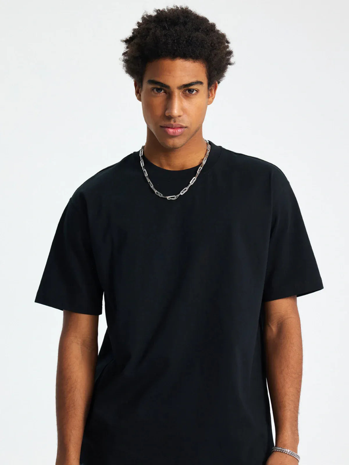 A man with short curly hair wears a Custom Anime Character Black T-Shirt (230GSM 100% cotton) and a silver chain necklace, standing against a light background.