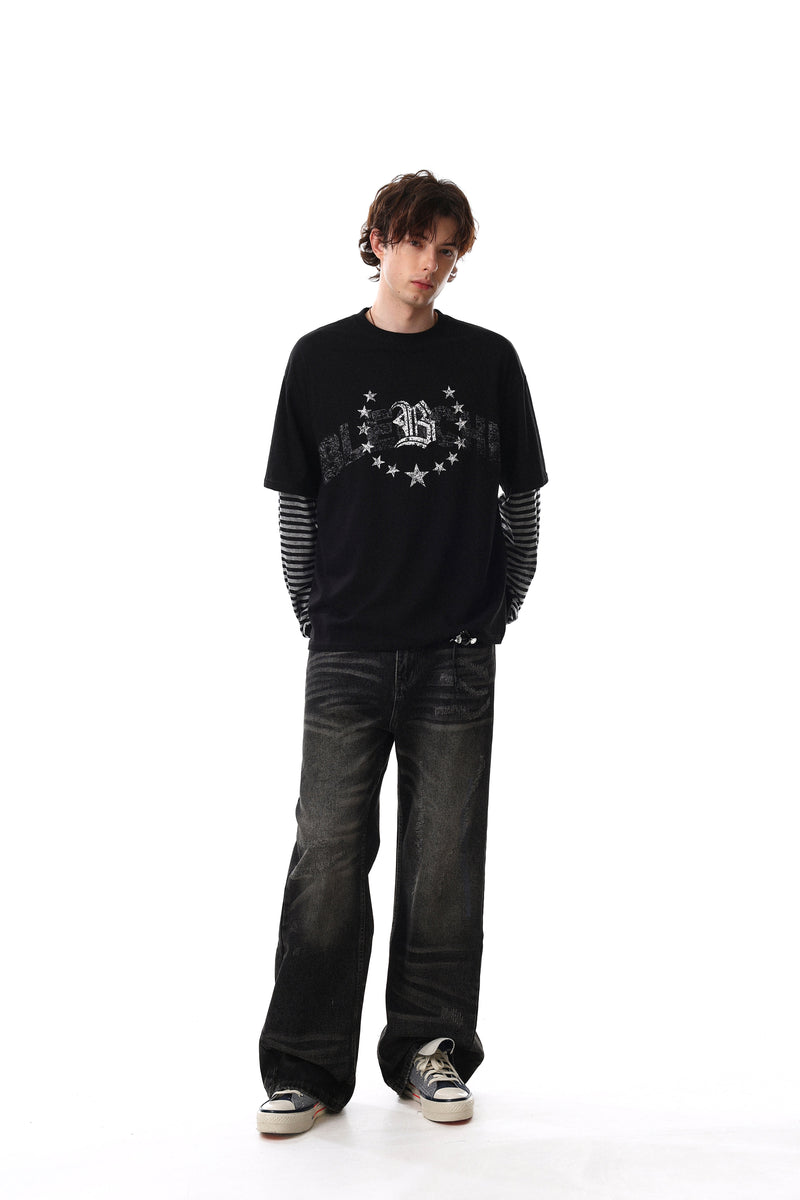 Model wearing black graphic long sleeve tee with striped sleeves and dark jeans, relaxed full-body view