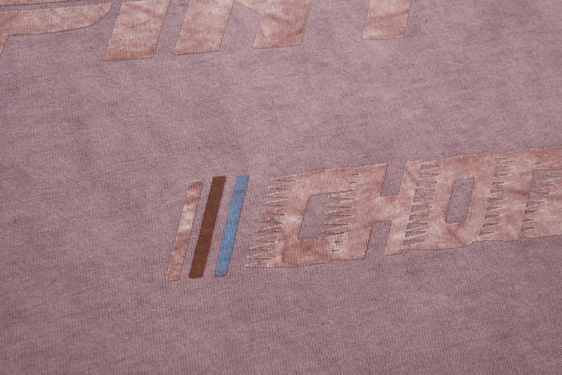 Close-up of a washed pink racing graphic tee with faded retro motorsport lettering and striped print details