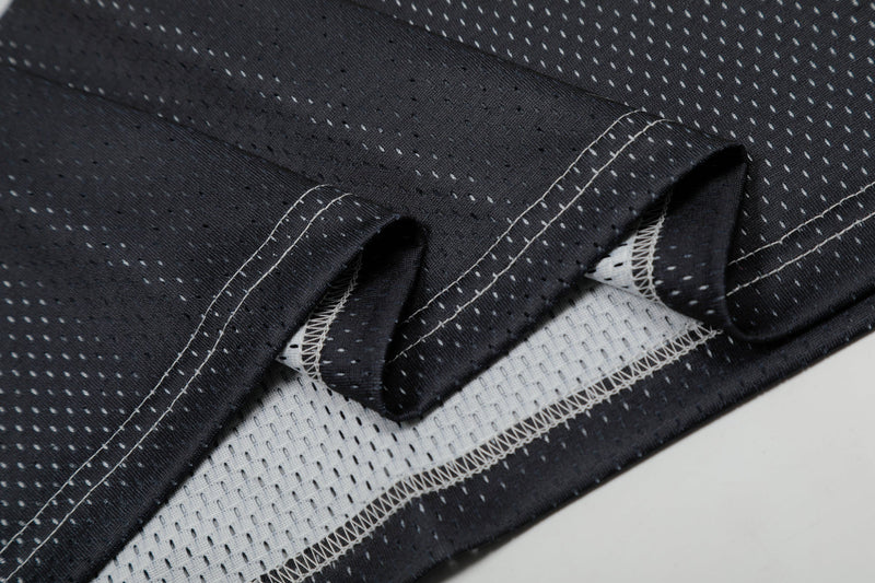 Close-up of black mesh football jersey hem with white stitching and perforated lining details