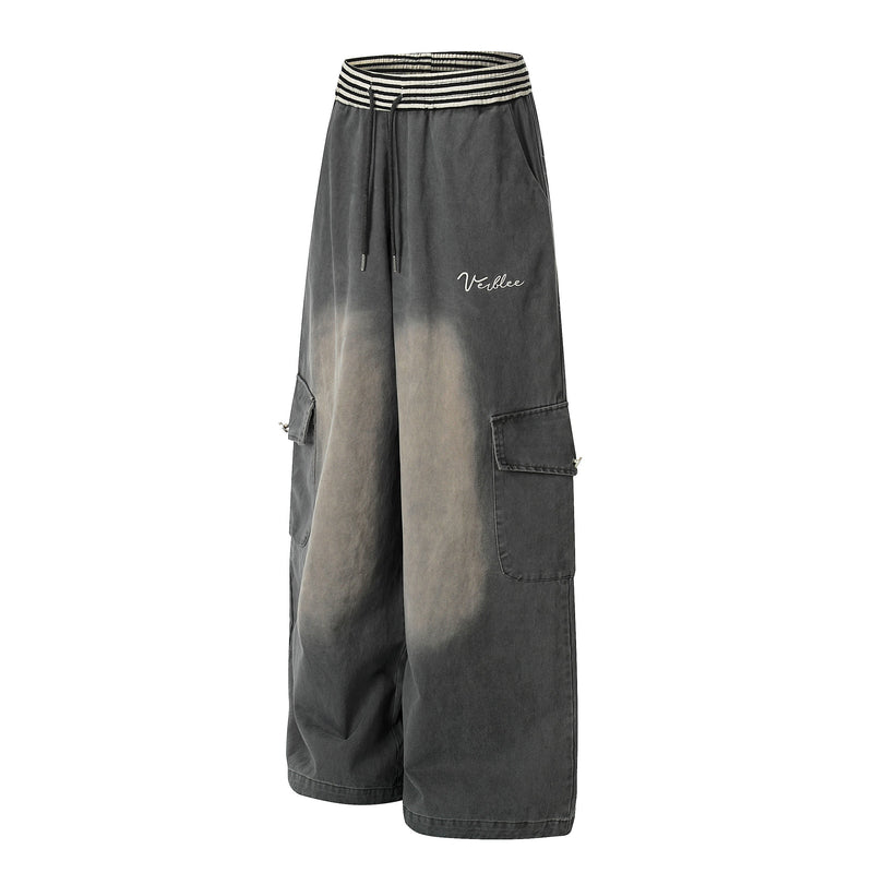 Angled front view of washed charcoal cargo pants with wide legs, striped waistband, and side flap pockets