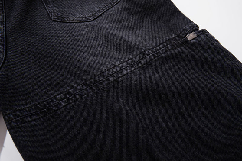 Close-up of dark wash jeans side seam with topstitched panel and metal tab