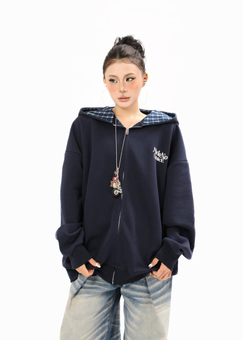 Model wearing a navy zip-up hoodie with blue plaid hood lining, logo print, and pendant necklace