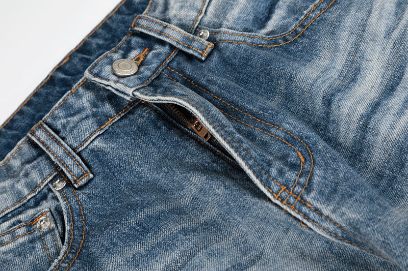 Close-up of front jeans pocket, button, and orange stitching on faded blue denim