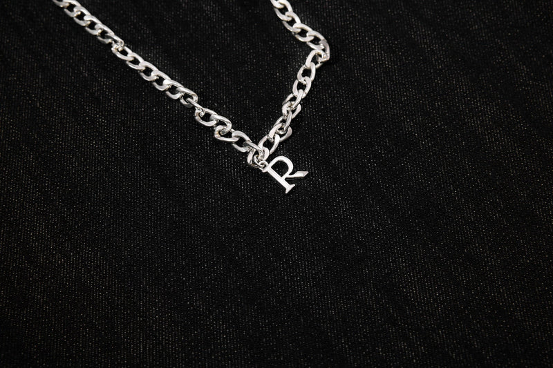 Close-up of silver chain detail with letter charm on black denim