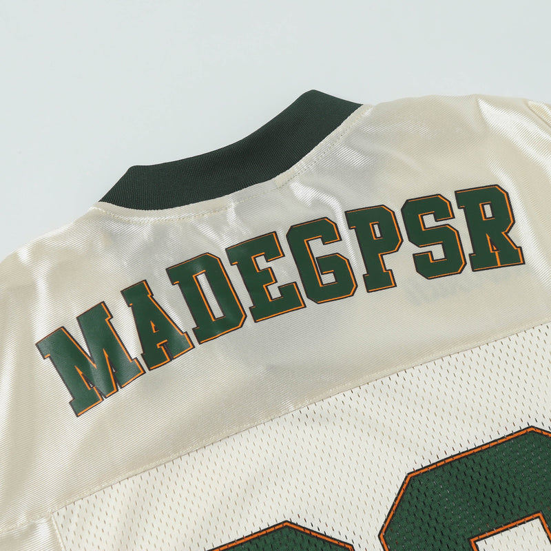 Close-up of a cream retro football jersey tee with dark green collar and MADCPSR lettering in varsity style