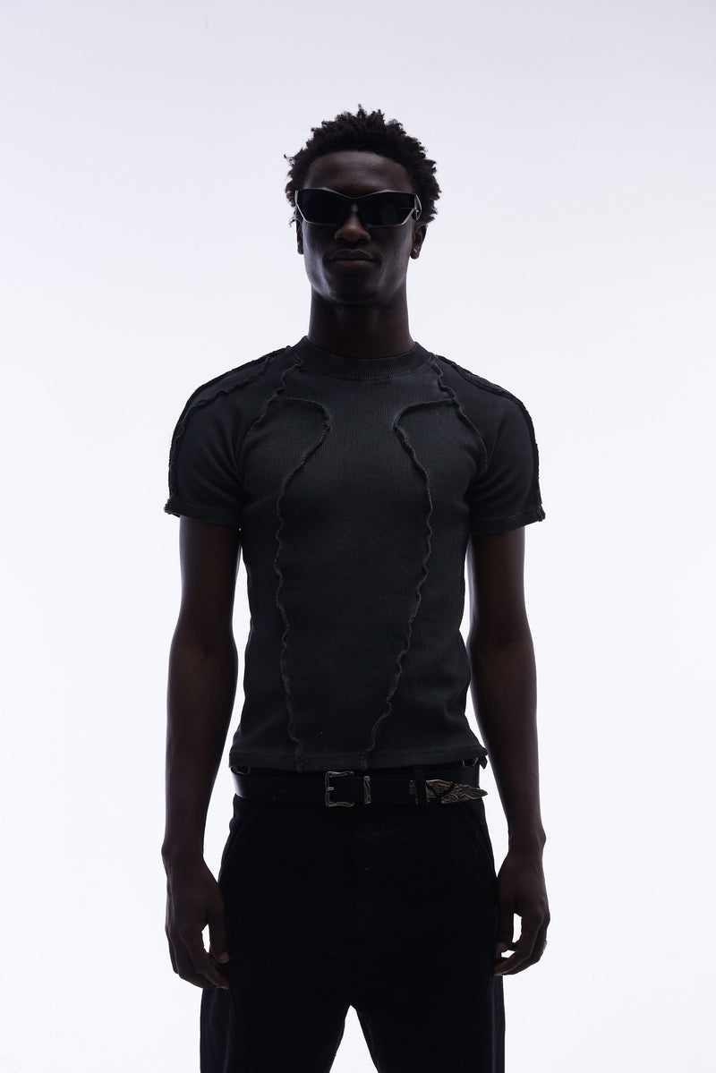Black deconstructed compression tee with raw seam detailing, worn by a model with sunglasses against a white background