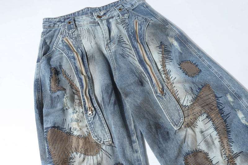 Front upper view of distressed patchwork denim pants with dual zippers and raw patches