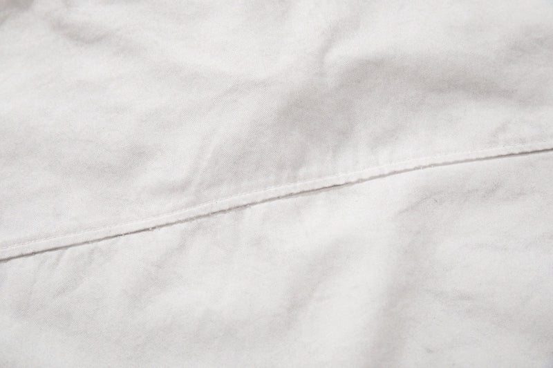 Close-up of an off-white short sleeve shirt with subtle seam detail and textured fabric weave