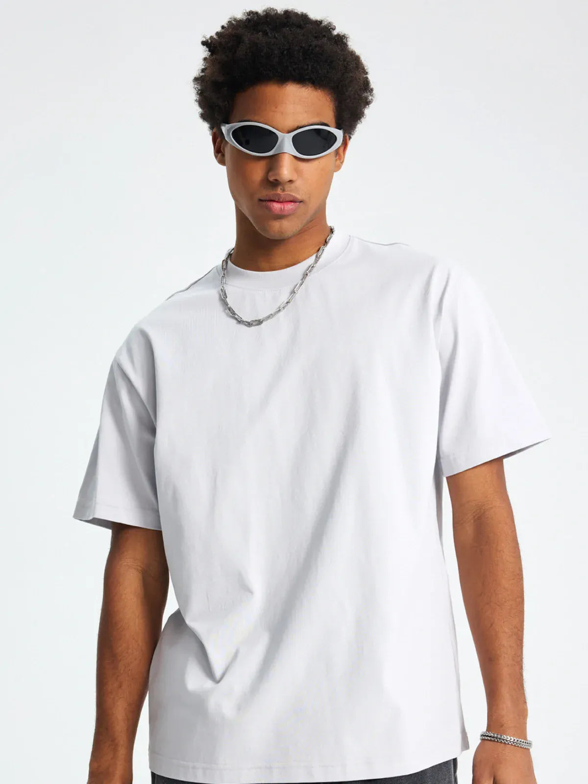 A man wearing a Custom Anime Character White T-Shirt - Personalized 230GSM 100% Cotton Tee, a silver chain necklace, silver bracelet, and oval sunglasses stands against a plain background.