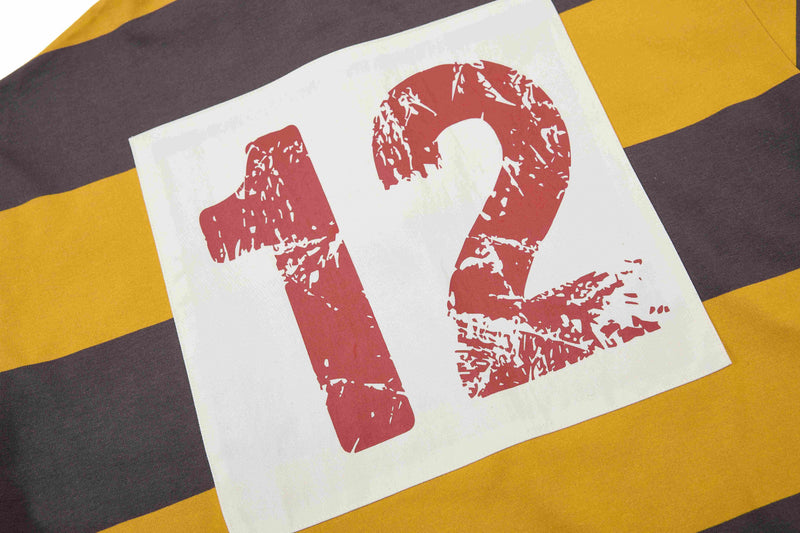 Close-up of a rugby polo with bold mustard and dark brown stripes and a distressed red 12 graphic on a white patch