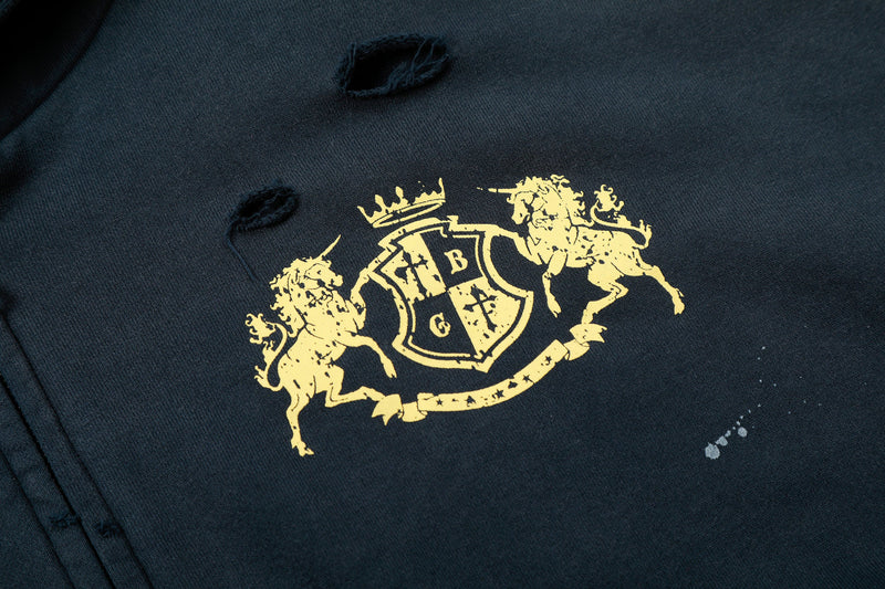Close-up of gold crest graphic on navy hoodie with distressed hole above