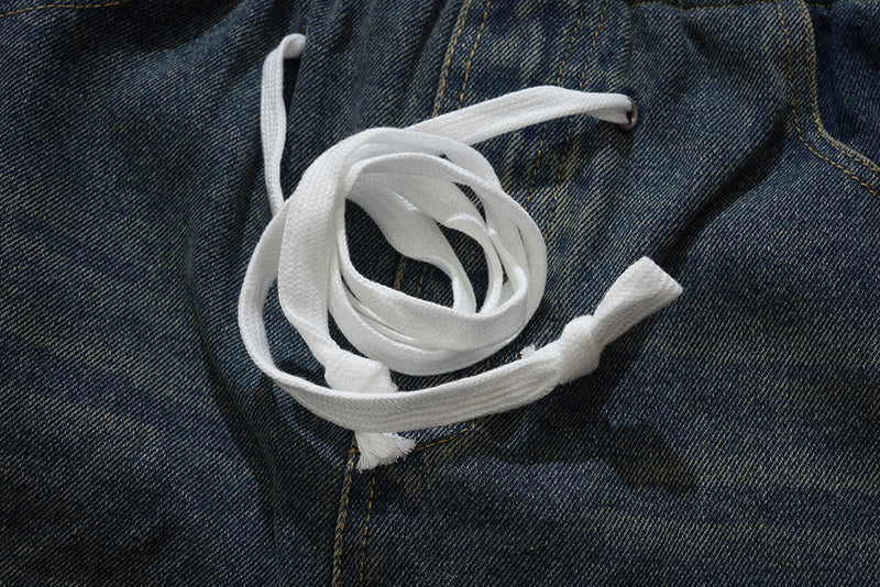 Close-up of white drawstring ties on dark wash denim pants