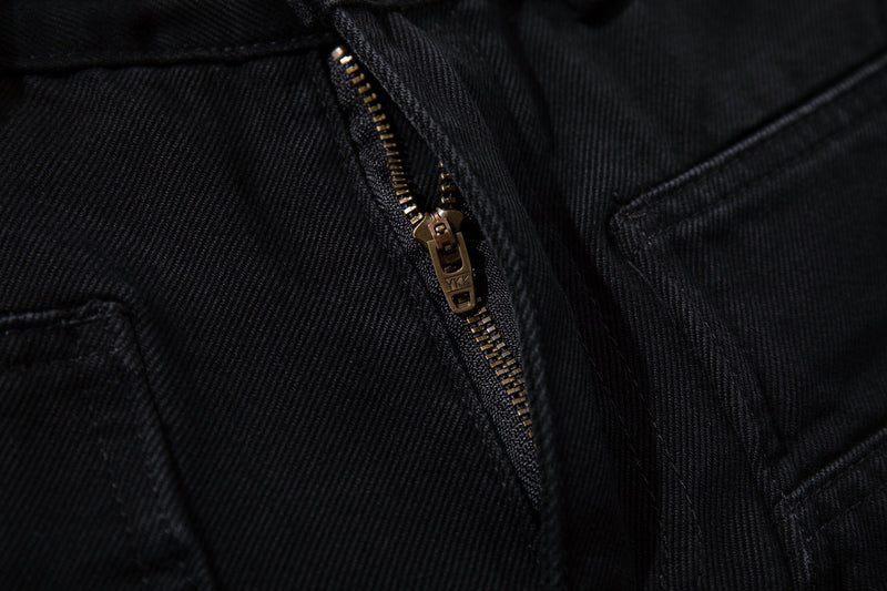 Close-up of black denim fly with bronze zipper and diagonal seam details