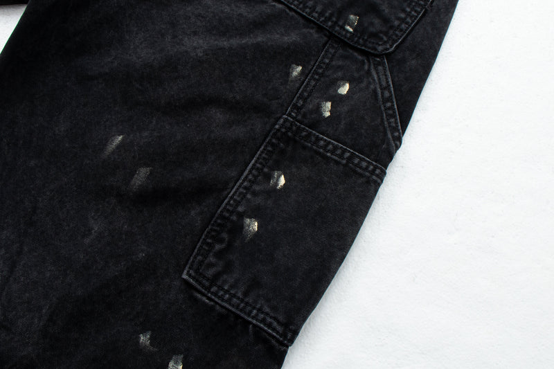 Close-up of black denim side seam and utility pocket with paint specks