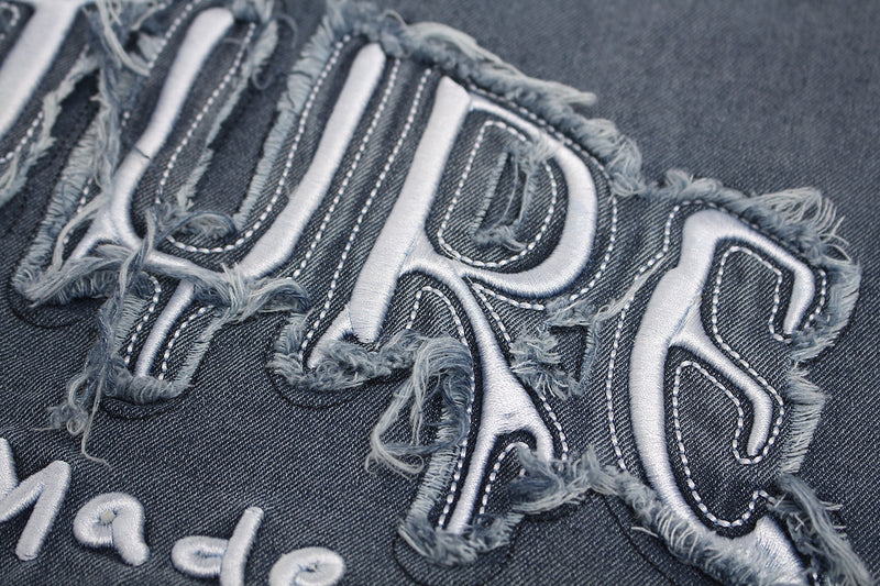 Close-up of distressed denim patch lettering on a vintage washed streetwear T-shirt with frayed edges and white stitching
