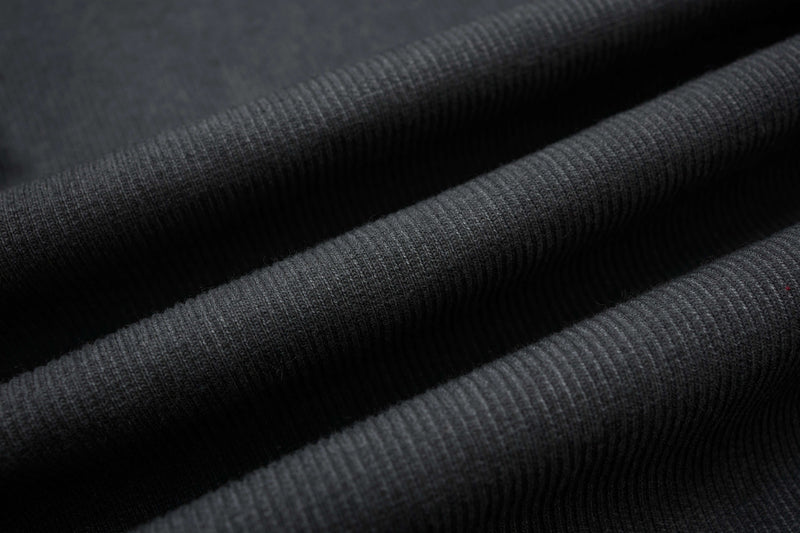 Close-up of black ribbed compression fabric with raw seam texture and deconstructed streetwear styling