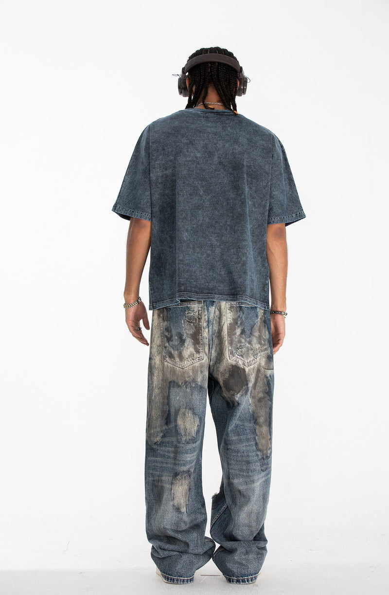 Oversized faded black graphic tee worn with distressed wide-leg jeans, shown from the back on a male model