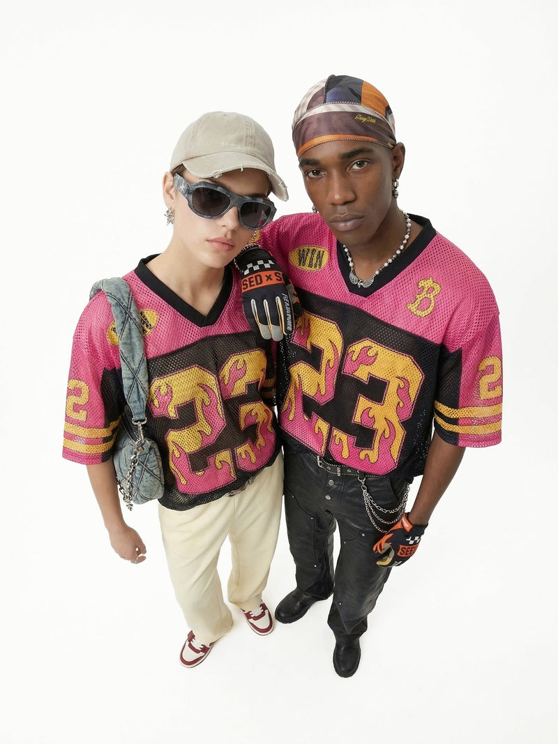 Two models wearing pink mesh jersey streetwear tops with bold flame graphics and oversized football-inspired numbers