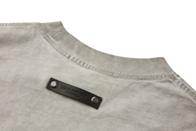 Close-up of a vintage washed beige tee with ribbed collar and black rivet detail on heavyweight cotton fabric