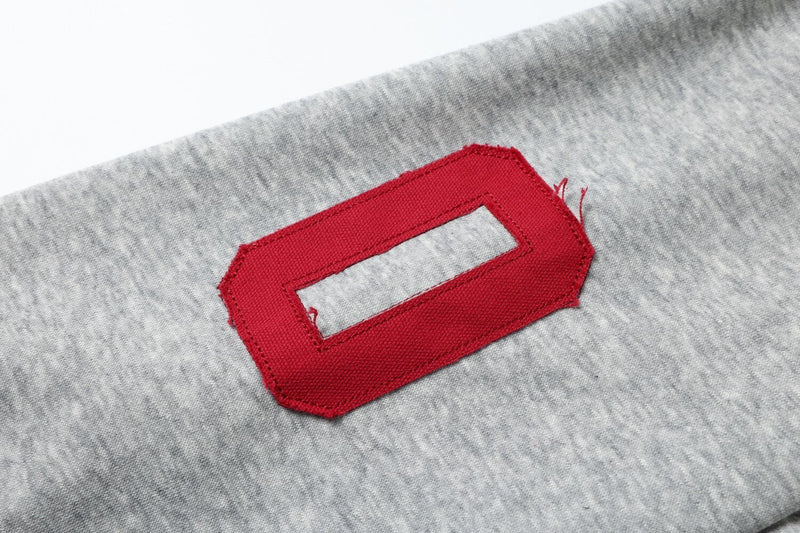 Close-up of red embroidered TAP letter on light gray hoodie sleeve