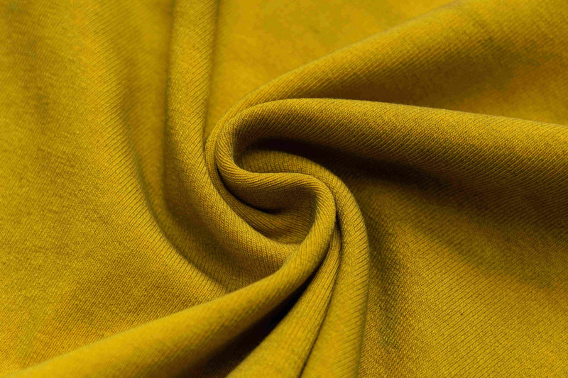 Close-up of mustard yellow washed cotton tee fabric with soft folds and textured knit finish