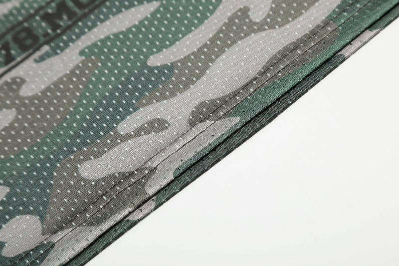 Close-up of green camo mesh jersey fabric with stitched hem and breathable dotted texture on white background