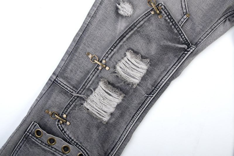 Mid-leg close-up of grey flare jeans with distressed patches, buckles, and grommet trim