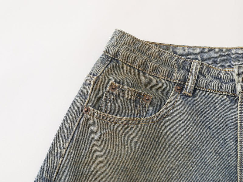 Close-up of the front waist and pocket on faded blue denim pants with curved stitching and rivet details