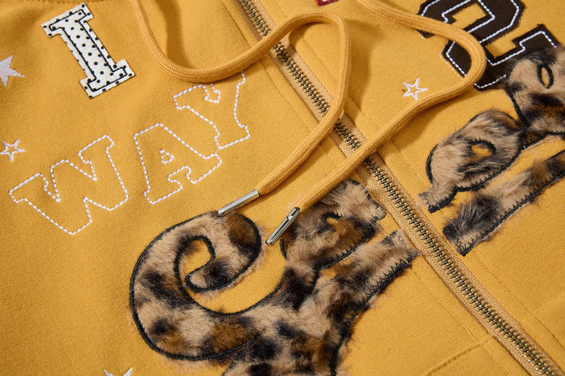 Close-up of mustard yellow hoodie chest graphic, zipper, and drawstrings