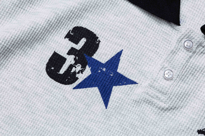 Close-up of a white textured polo tee with black collar, embroidered black number 3, and blue star graphic