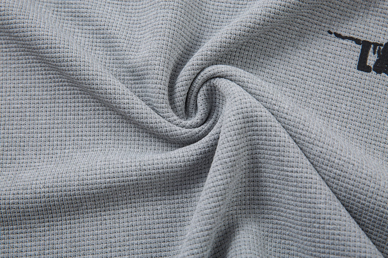 Close-up of gray waffle knit fabric with black graphic print on a Seakoff streetwear half-zip neck t-shirt