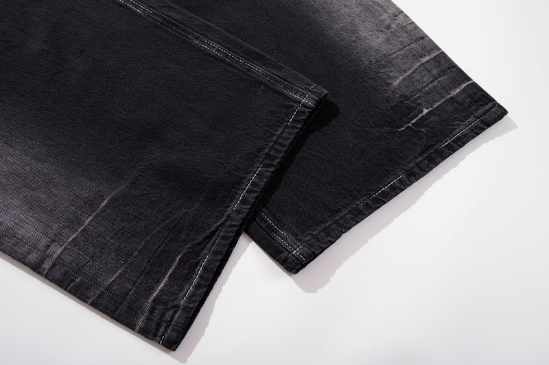 Close-up of the wide hem on dark wash jeans with faded creases and topstitching