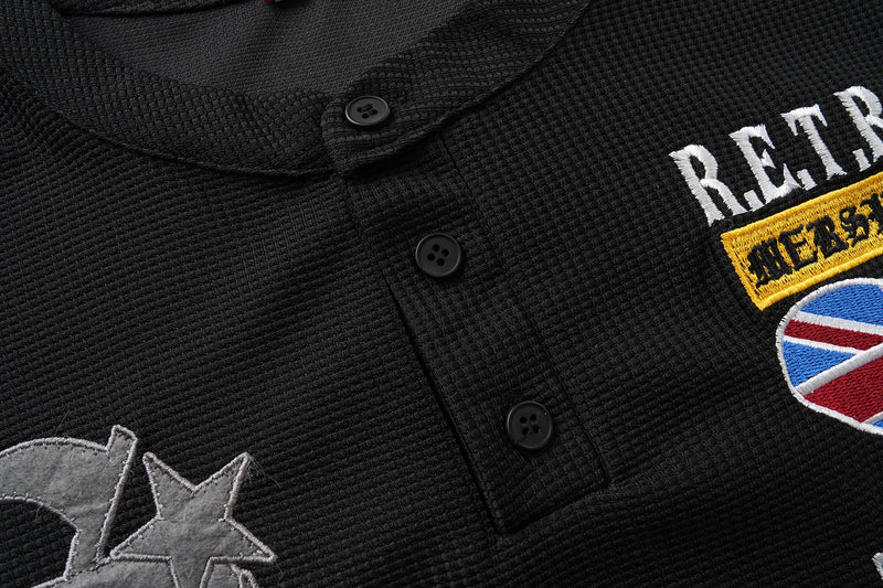 Close-up of black Henley buttons and partial retro embroidery on waffle-knit fabric