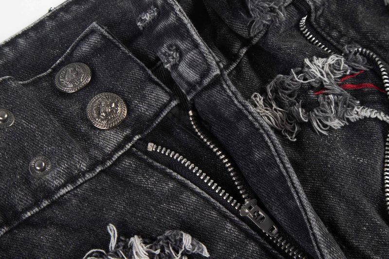 Close-up of black denim with silver zipper trim, frayed distressing, and metal button details