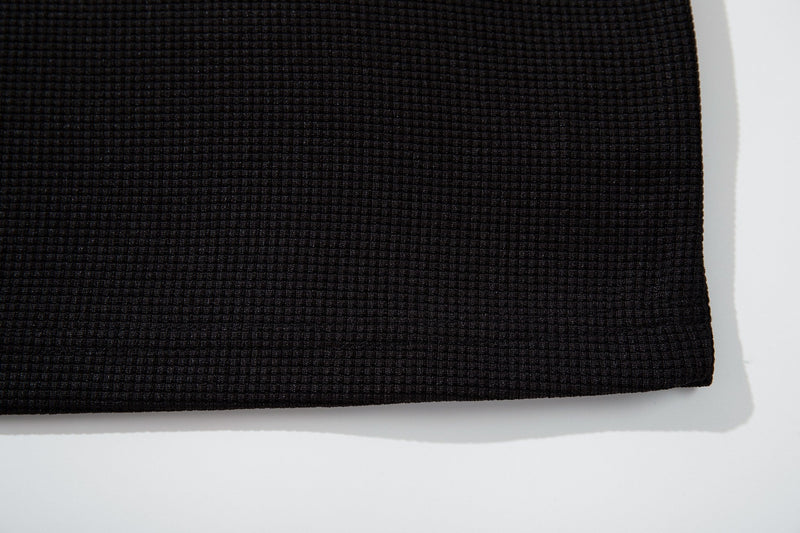 Close-up of black textured ringer T-shirt fabric with a subtle vintage waffle knit pattern and hem edge